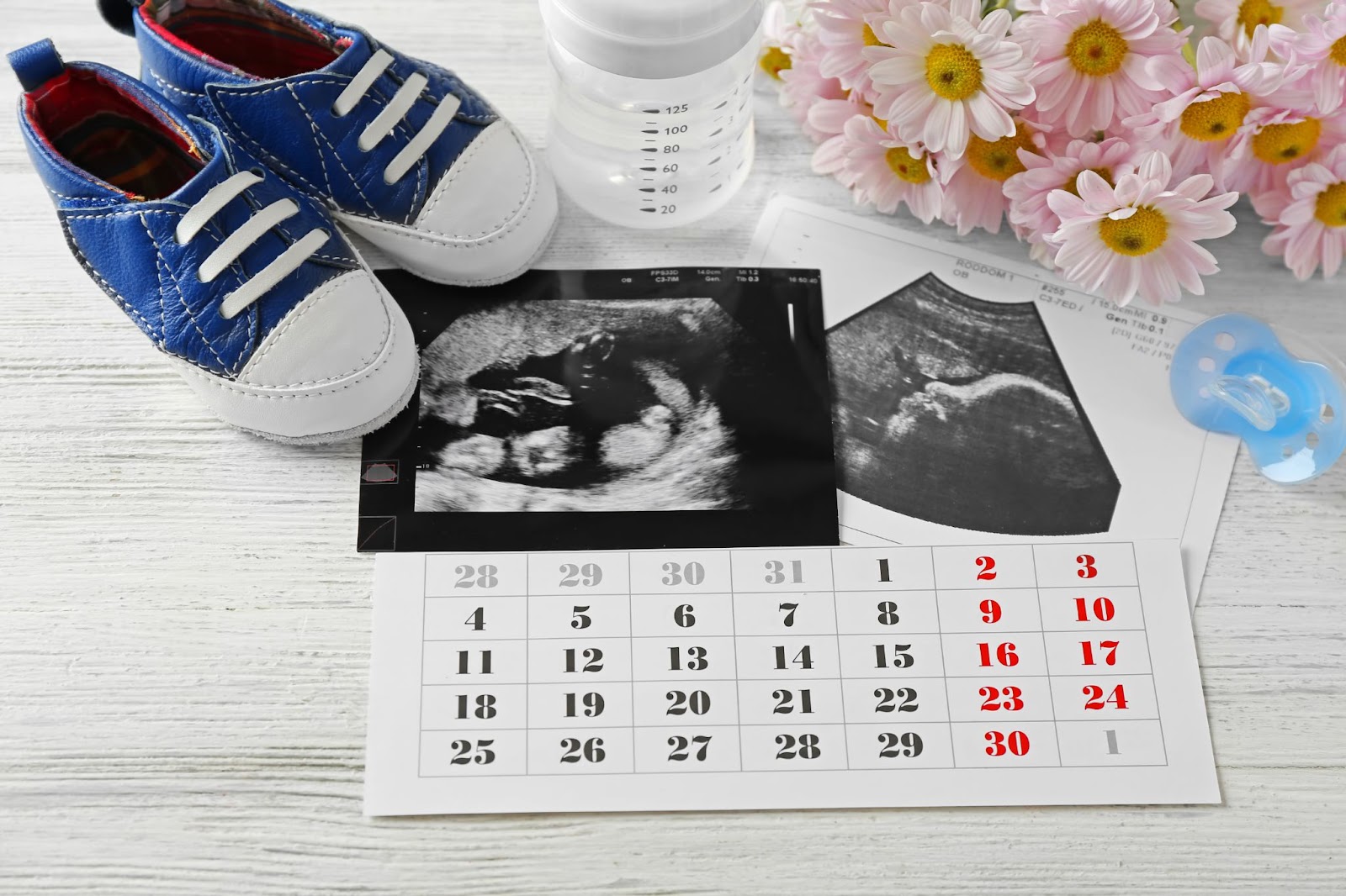 Pregnancy calendar alongside an ultrasound photo, infant shoes, and a baby bottle.